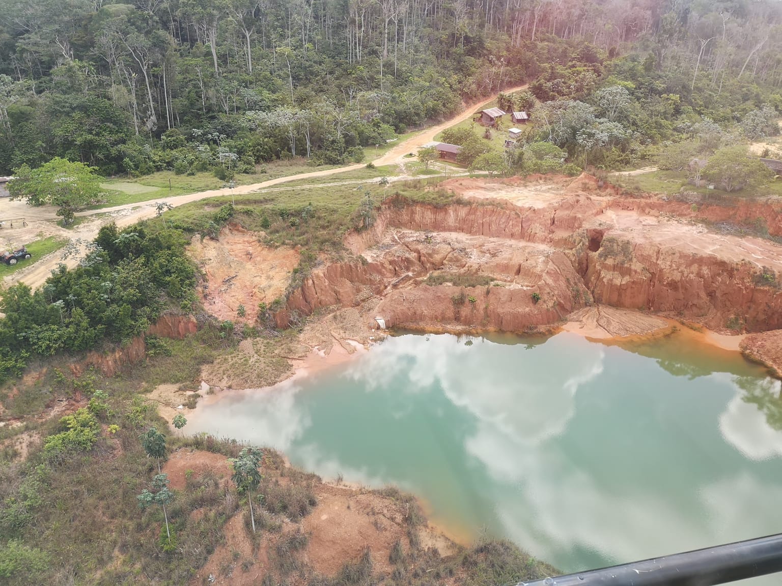 Aerial of a turquoise pond and the cut jungle road along the Jons Trend extension, Sela Creek