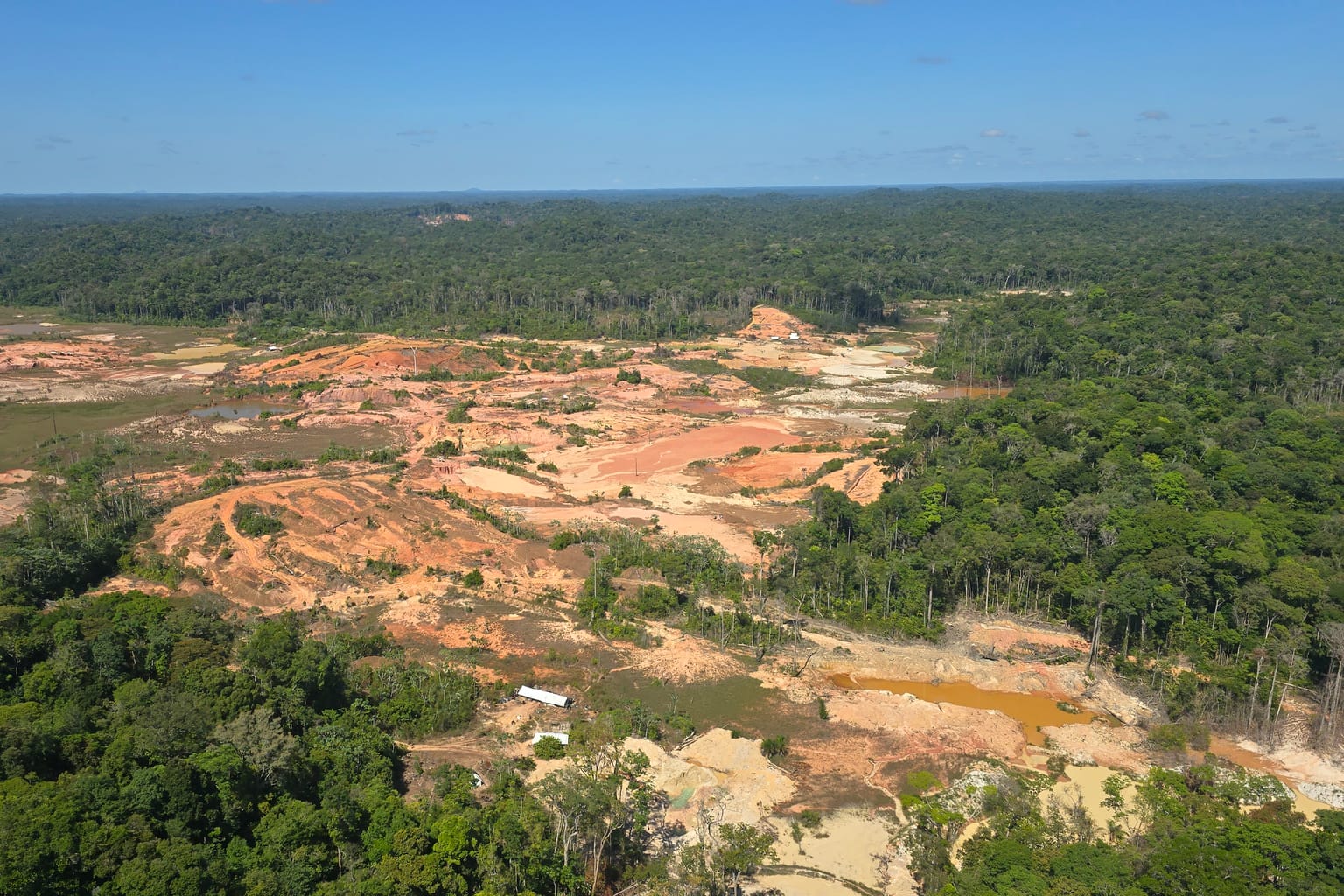 Aerial view over the Sela Creek artisanal gold workings and forested valley in sunlight, eastern Suriname