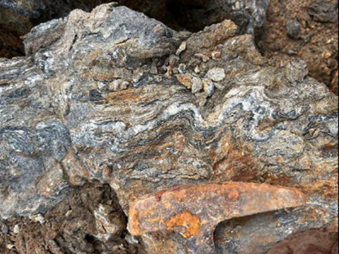 Deformed quartz veins in schist from the Golden Hand target, with a rock hammer for scale.